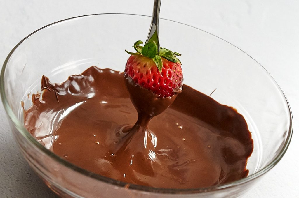 A single ripe strawberry being dipped into the melted chocolate. 