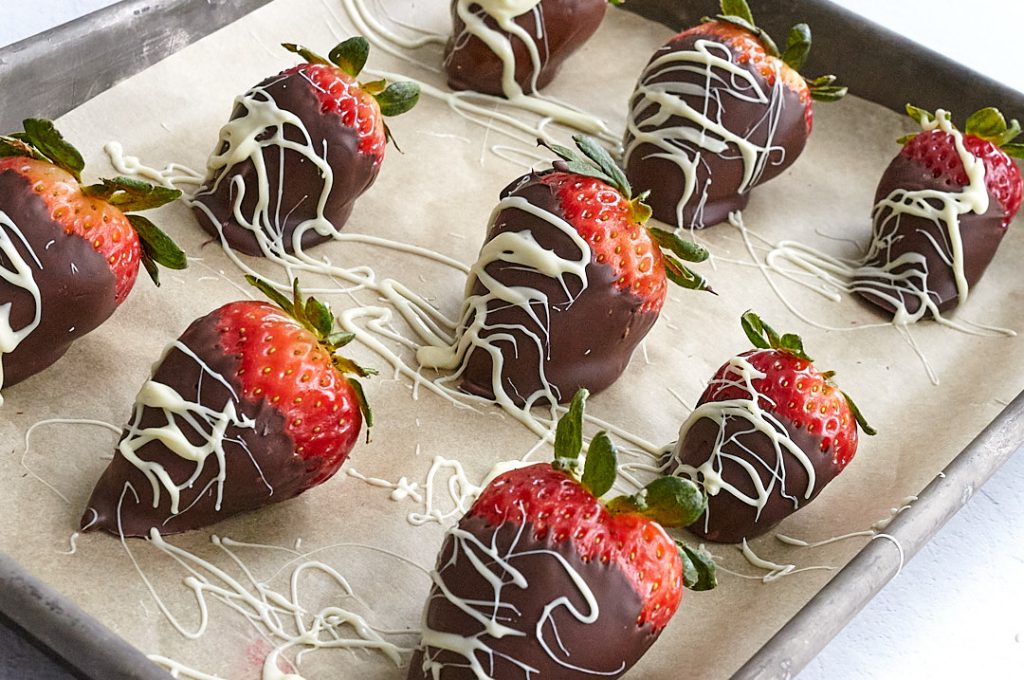 A tray of dark chocolate dipped strawberries, drizzled with white chocolate. 