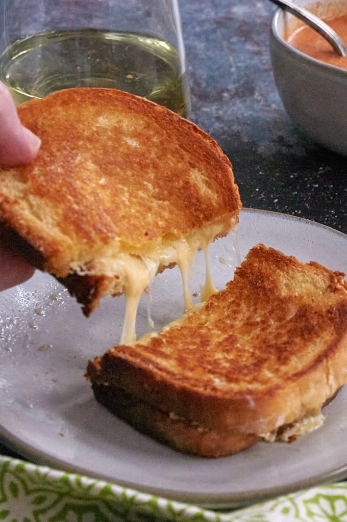 A grilled cheese sandwich sliced in half. A hand holds up half of the sandwich and strings of melted cheese are visible.